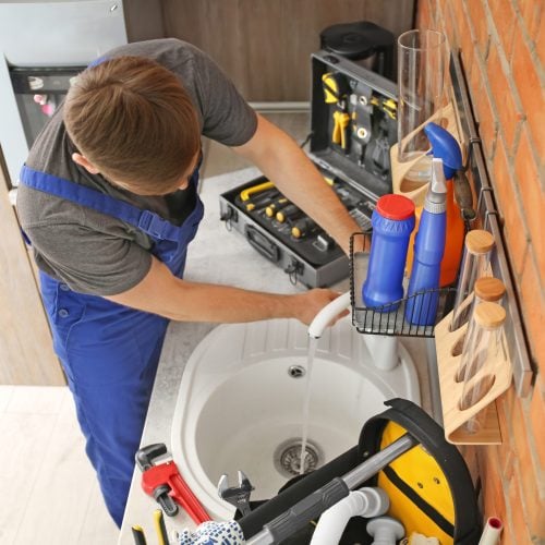 Professional plumber in uniform fixing kitchen sink